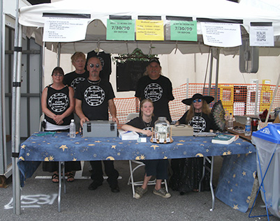 Volunteers in booth, wearing "Witches of Coven Oldenwilde" t-shirts