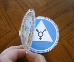 Folded lamen, top disc with state seal on outside held open to show bottom disc with blue restroom sign on inside