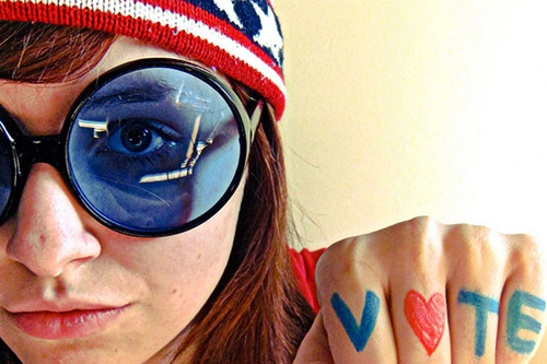 Young woman in blue sunglasses and patriotic ski cap shows fist with V Heart T E drawn on knuckles