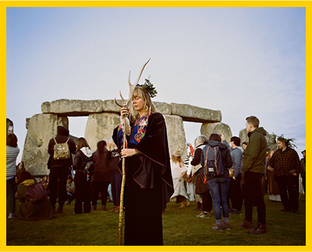 Pagans at Stonehenge, in foreground a blond priestess holding a stag-horn stang